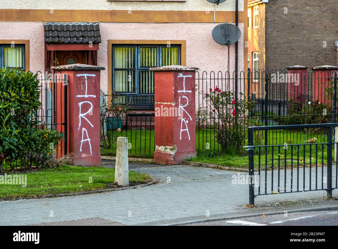 "IRA" graffiti has been spray-painted on two gate pillars in front of a house in the Bogside area of Londonderry, County Derry, Northern Ireland. Rose bushes bloom in the fenced front garden behind them. Stock Photo