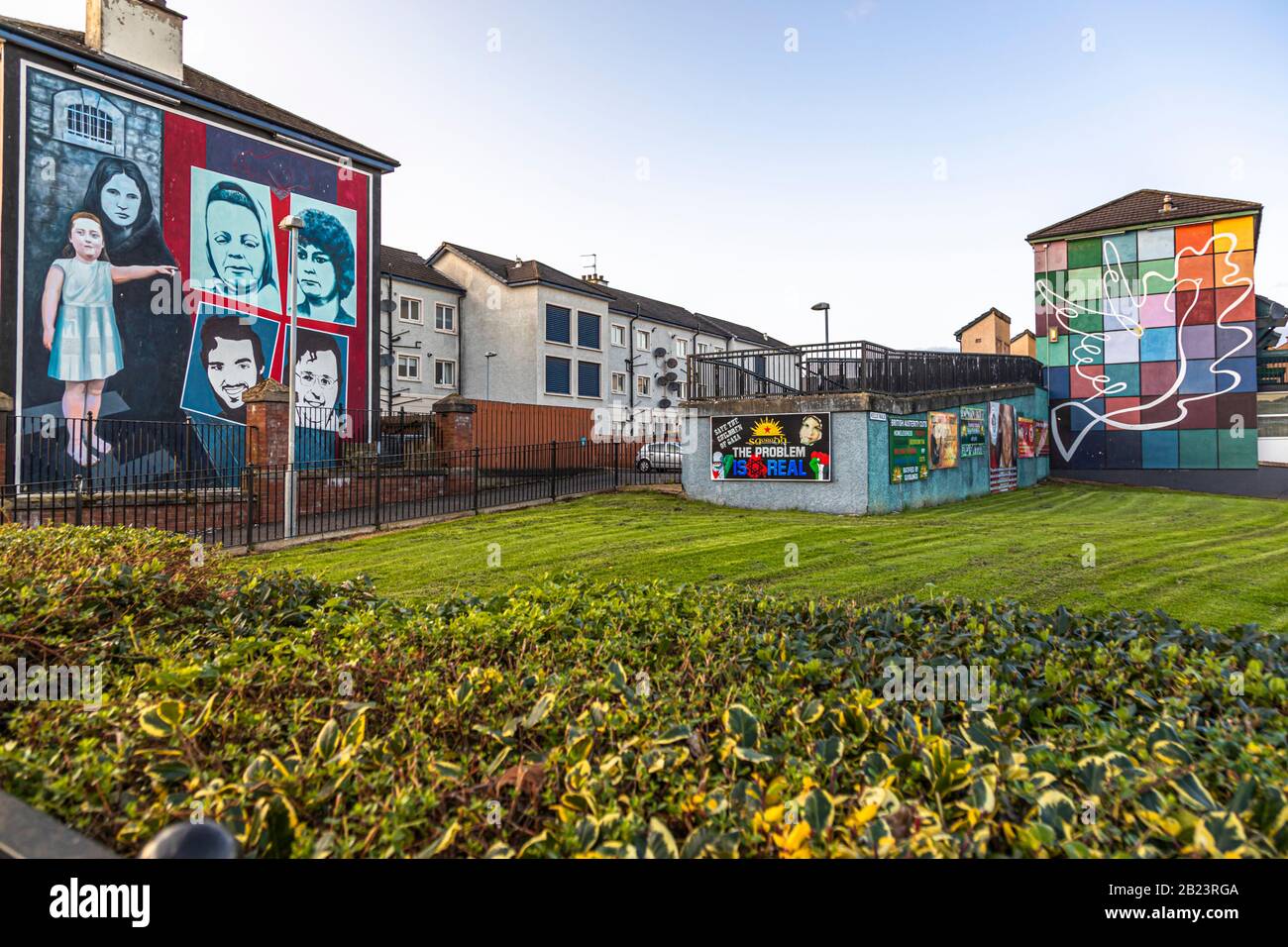 A mural showing a girl pointing to four portraits within a red-and-blue-framed panel stands on Rossville Street in the Bogside area of Londonderry, County Derry, Northern Ireland – possibly a memorial motif for victims of the Northern Ireland conflict ("the Troubles", 1968–1998). To its right stands the chequerboard "Peace Mural" with its white dove, the final work in the Bogside Artists' "People's Gallery" (unveiled 2004). A low wall bearing political posters links the two buildings. Stock Photo