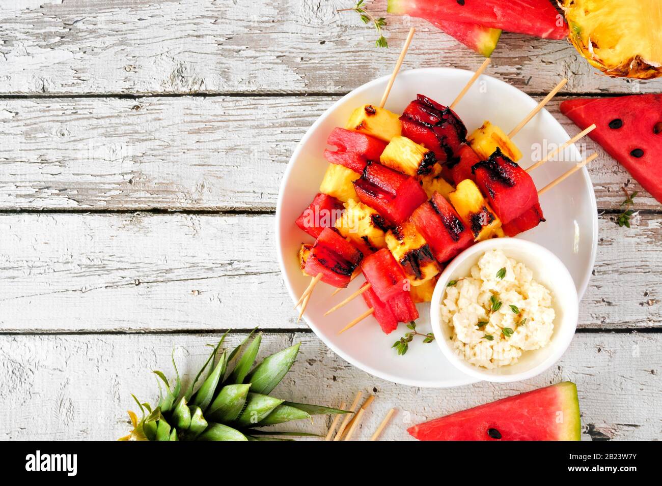 Grilled watermelon and pineapple fruit skewers with feta. Above view on a white wood table. Summer food concept. Stock Photo