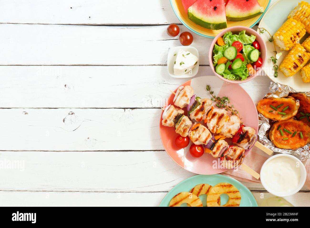 Summer BBQ or picnic food side border. Selection of grilled meat, fruits, salad and potatoes. Top view over a white wood background. Copy space. Stock Photo