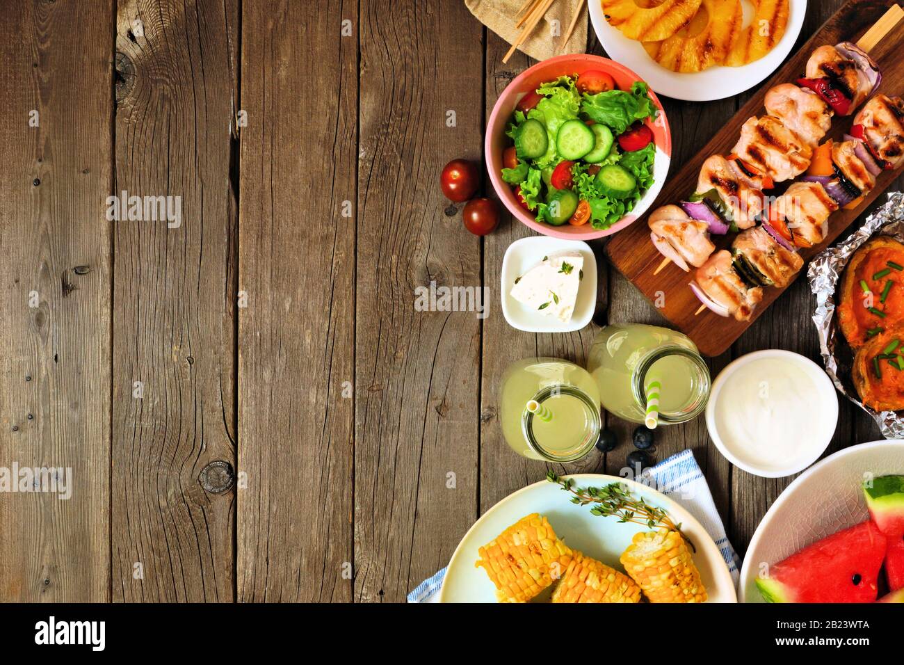 Summer BBQ or picnic food side border. Selection of grilled meat, fruits, salad and potatoes. Top view over a rustic wood background. Copy space. Stock Photo