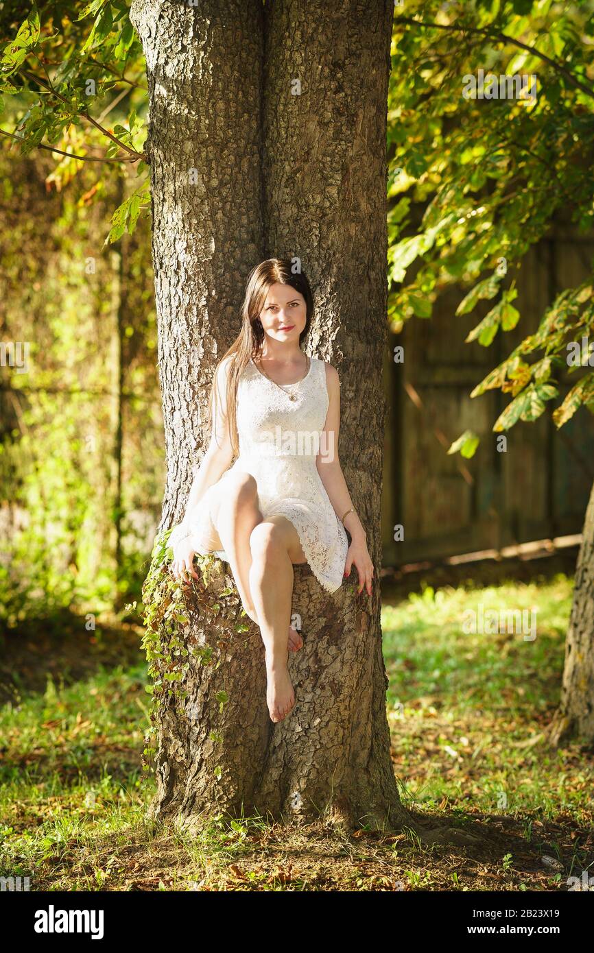 Beautiful happy girl in white dress sitting on a tree. Forest nymph Stock  Photo - Alamy