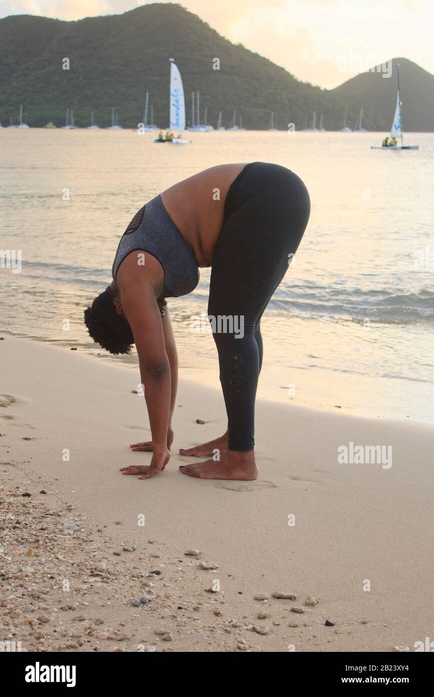 African lady with natural hair exercising stretching on the beach wearing a sports bra and black tights burning belly fat and staying fit and healthy Stock Photo