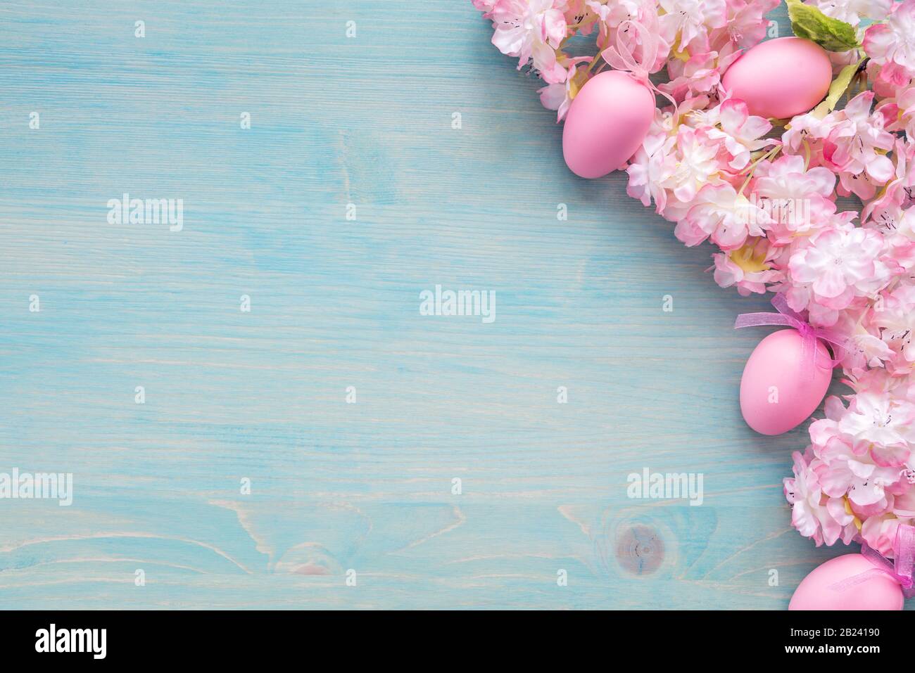 Spring Easter background of painted blue board with branch of flowering cherry covered with pink flowers and pink eggs as a border Stock Photo