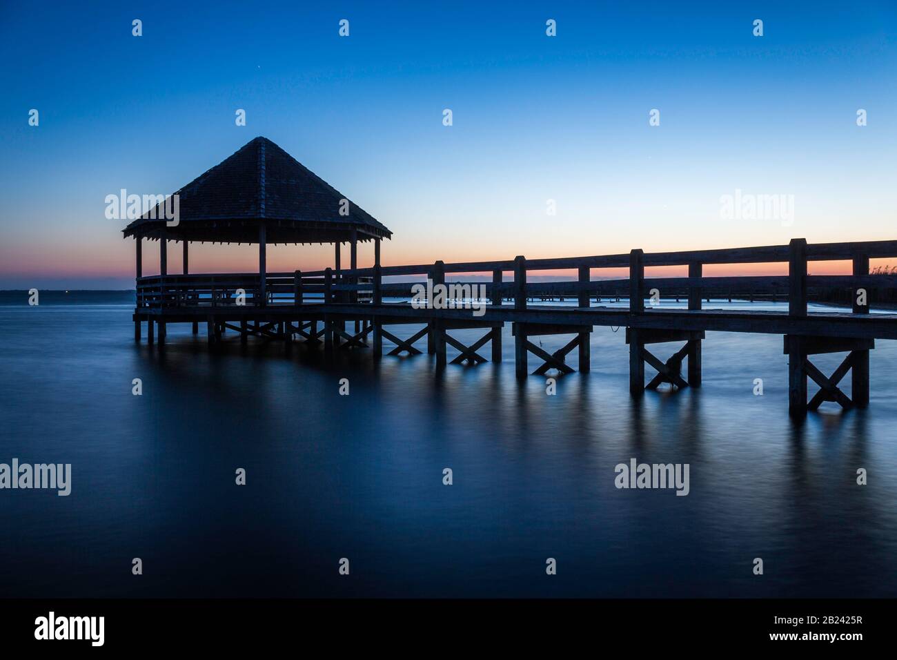 Blue sunset and water with wooden footbridge and thatched gazebo Stock Photo