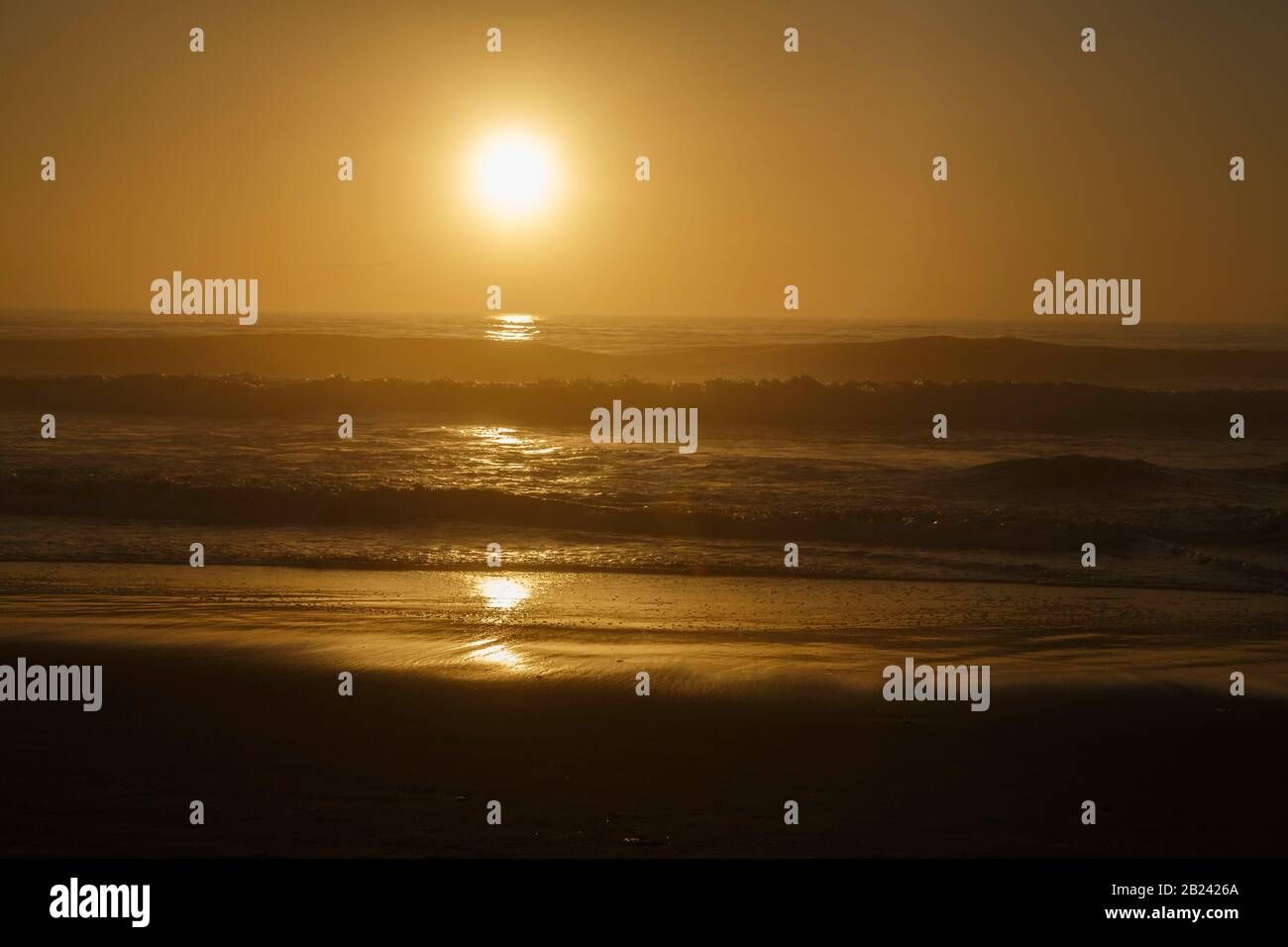 Hazy, warm ocean sunrise reflections on ocean surf. Stock Photo