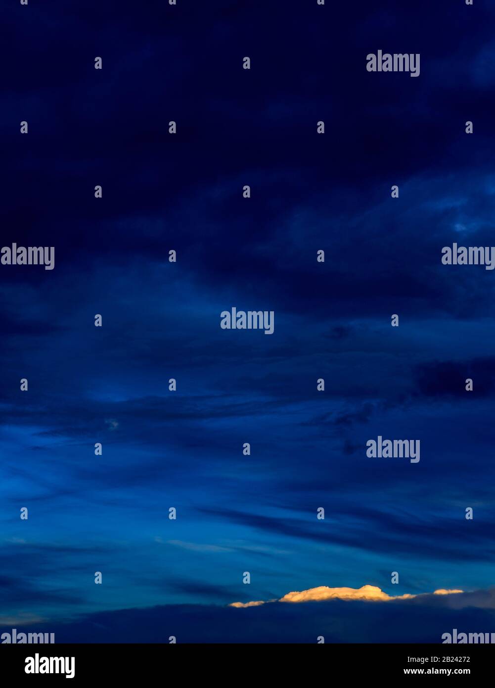 Vertical vivid blue nightscape of dramatic layered blues, pale moon and small bright cloud accent. Stock Photo
