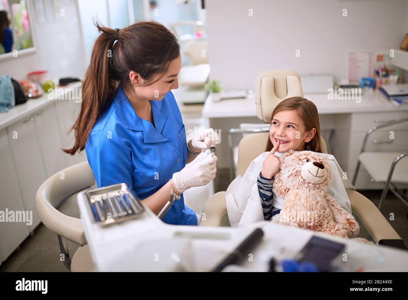 Smiling girl in dental chair showing tooth to dentist Stock Photo