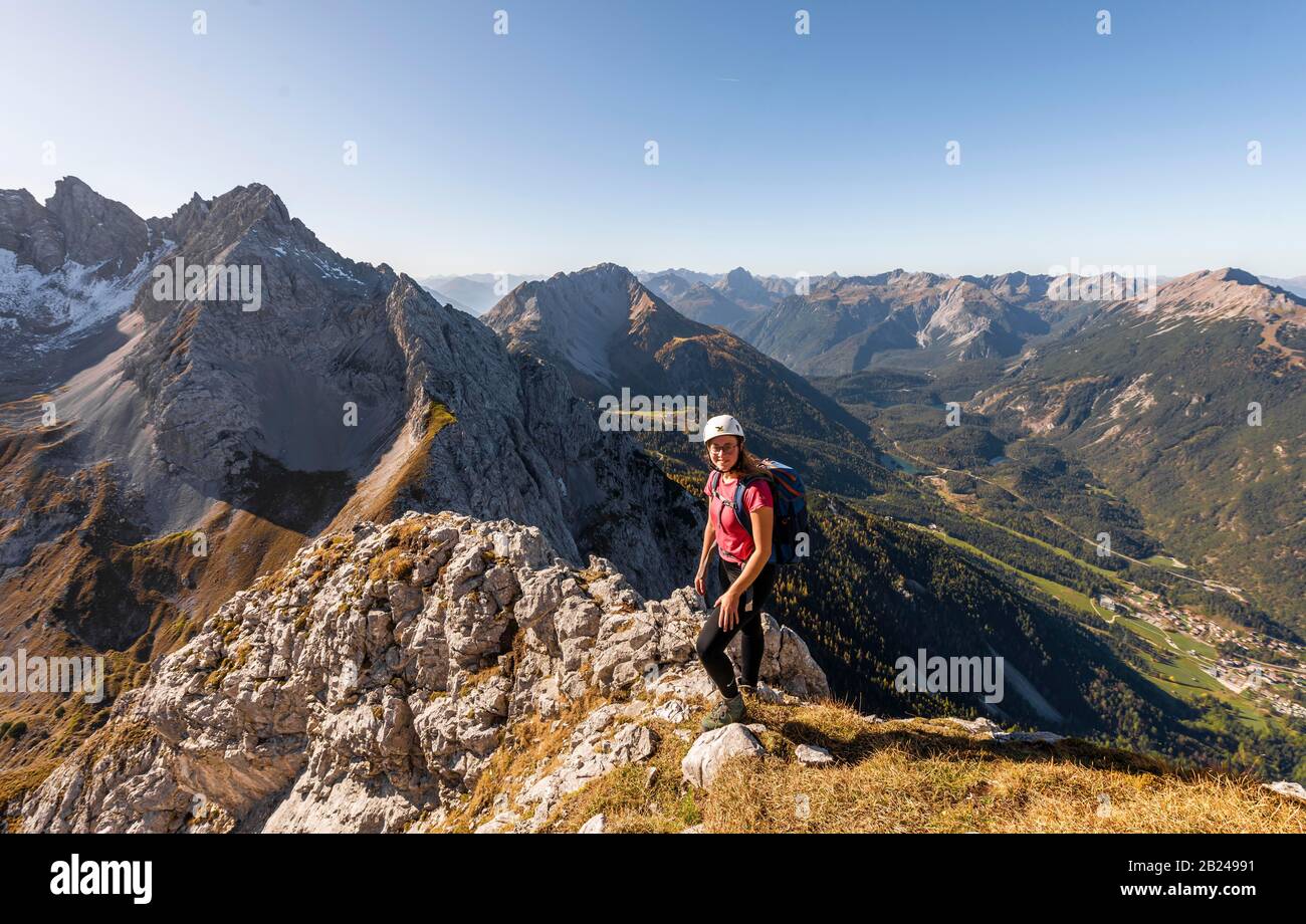 Young woman, mountaineer with climbing helmet looking at mountain landscape, hike to Ehrwalder Sonnenspitze, behind Gruenstein and western Stock Photo