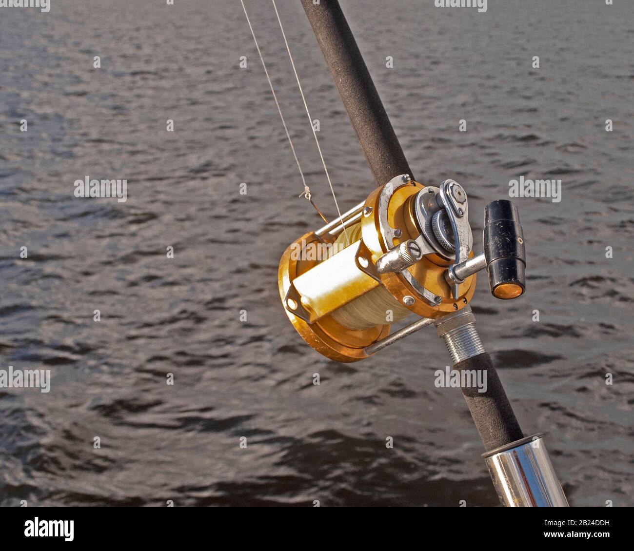 a gold coloured Big Game 50 wide fishing reel closeup in used condition.  Located in a rod holder aboard a yacht, ready to deploy Stock Photo - Alamy