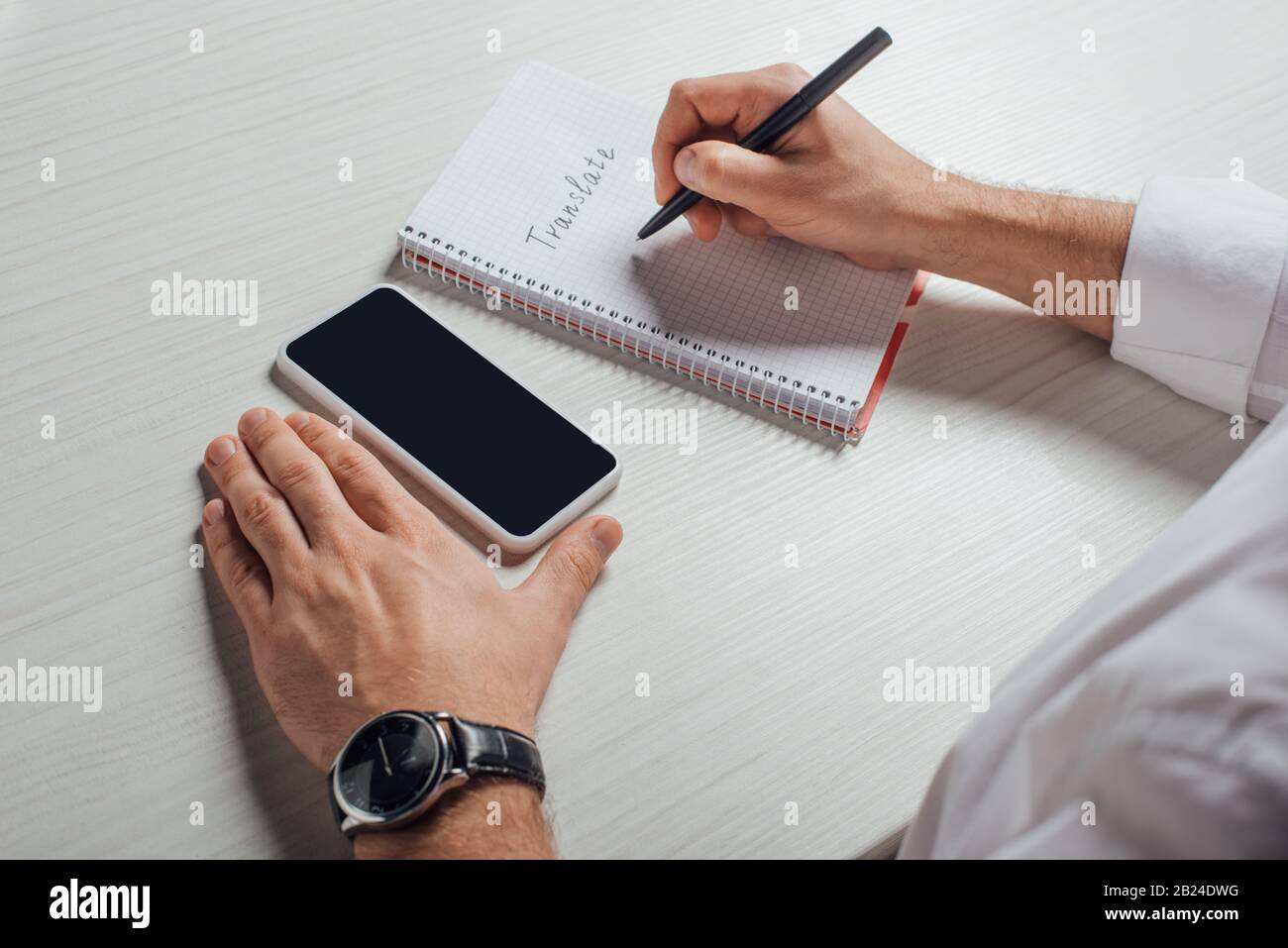 cropped view of translator writing in notepad with smartphone with