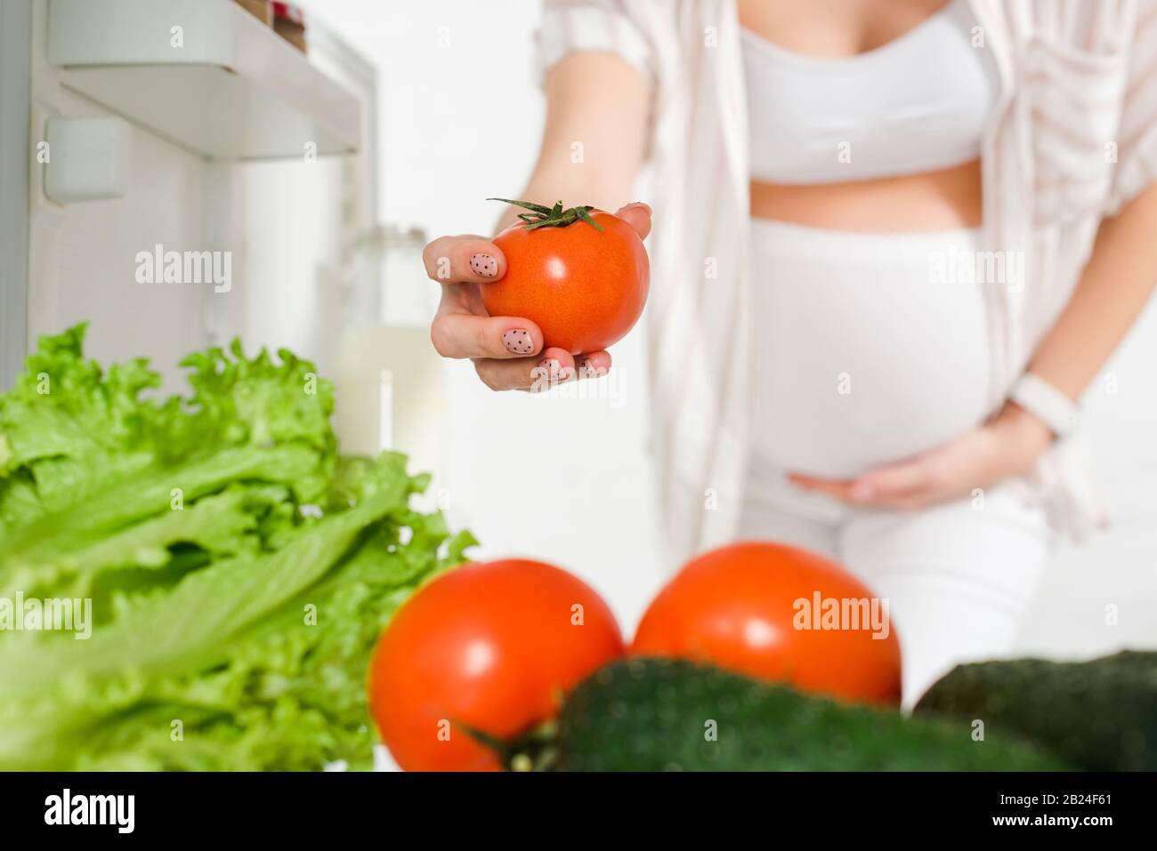 Selective focus of pregnant woman holding tomato near fresh vegetables