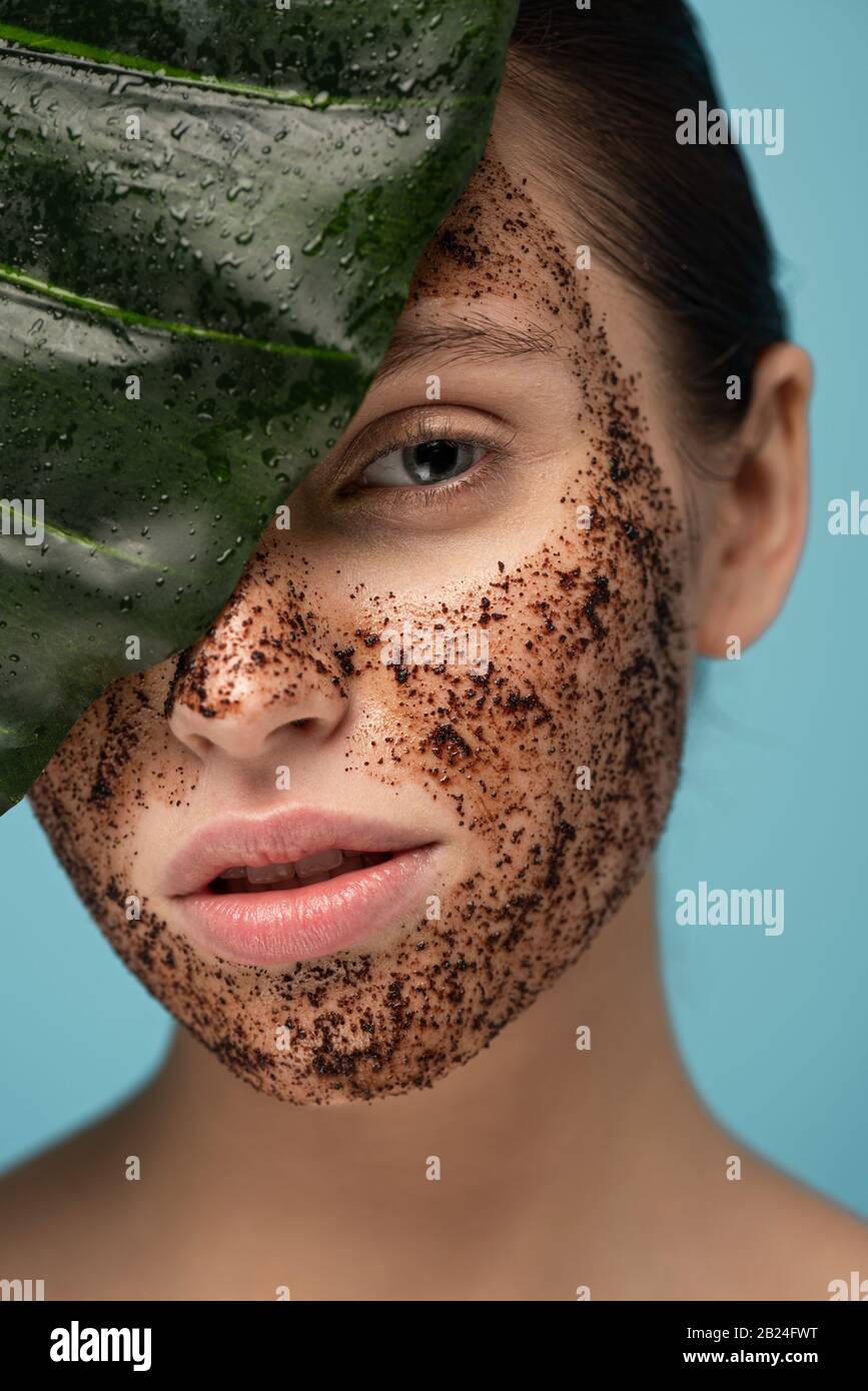 beautiful girl with coffee scrub on face, isolated on blue with leaf Stock Photo