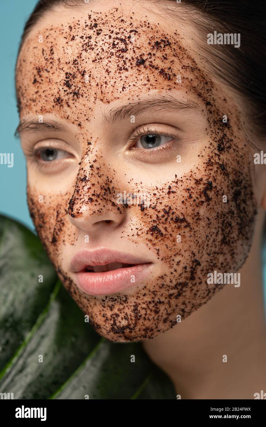 attractive girl with coffee scrub on face, isolated on blue with leaf Stock Photo