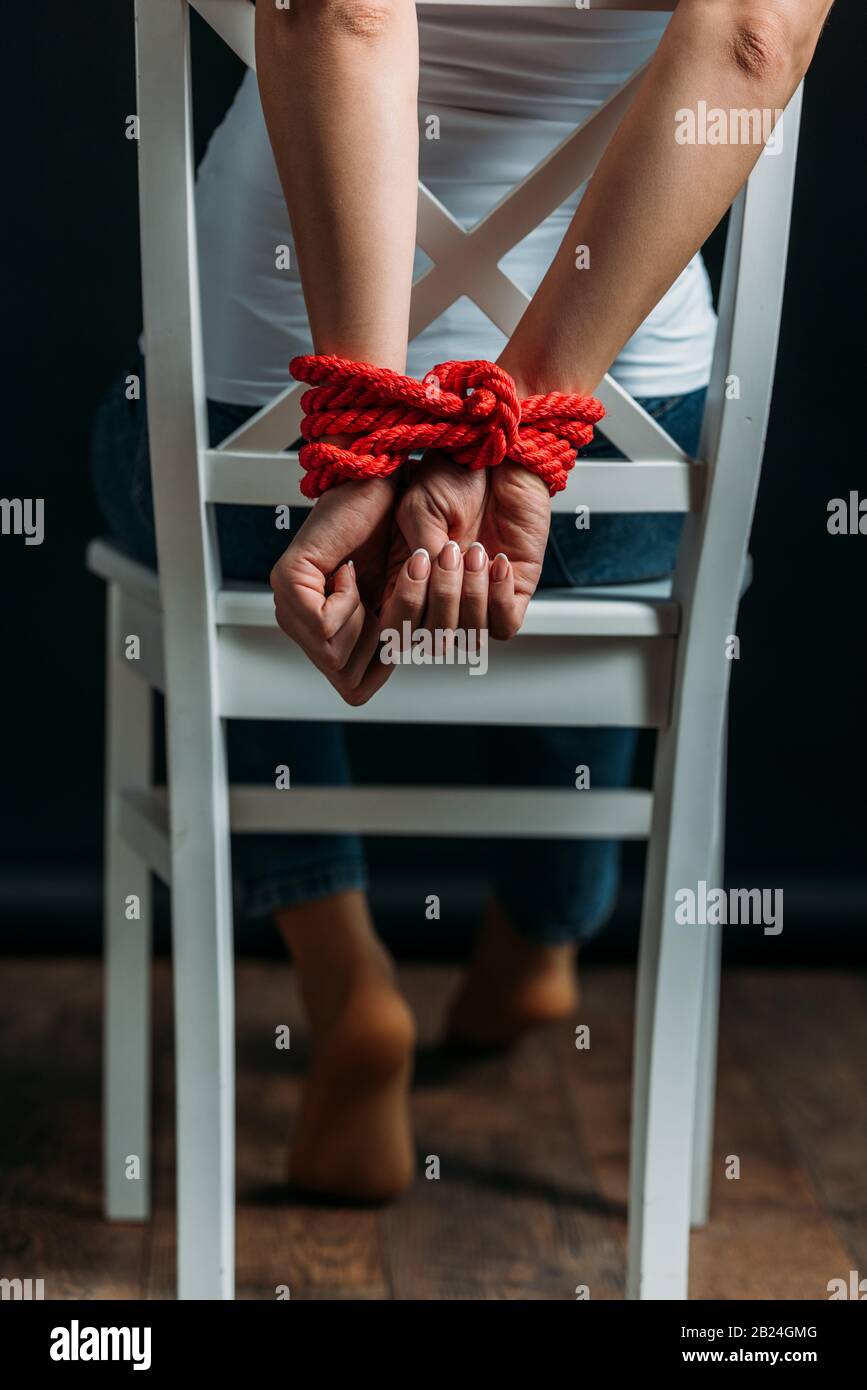 Cropped view of woman with tied hands on chair on black background Stock  Photo - Alamy