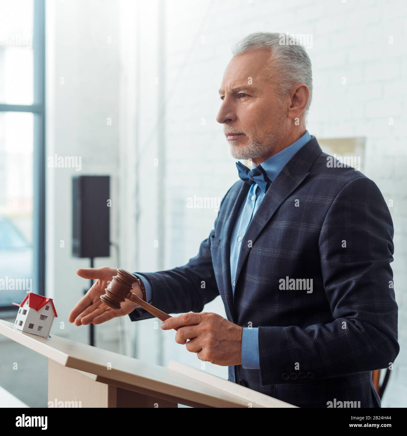 auctioneer pointing with hand at model of house and holding gavel ...
