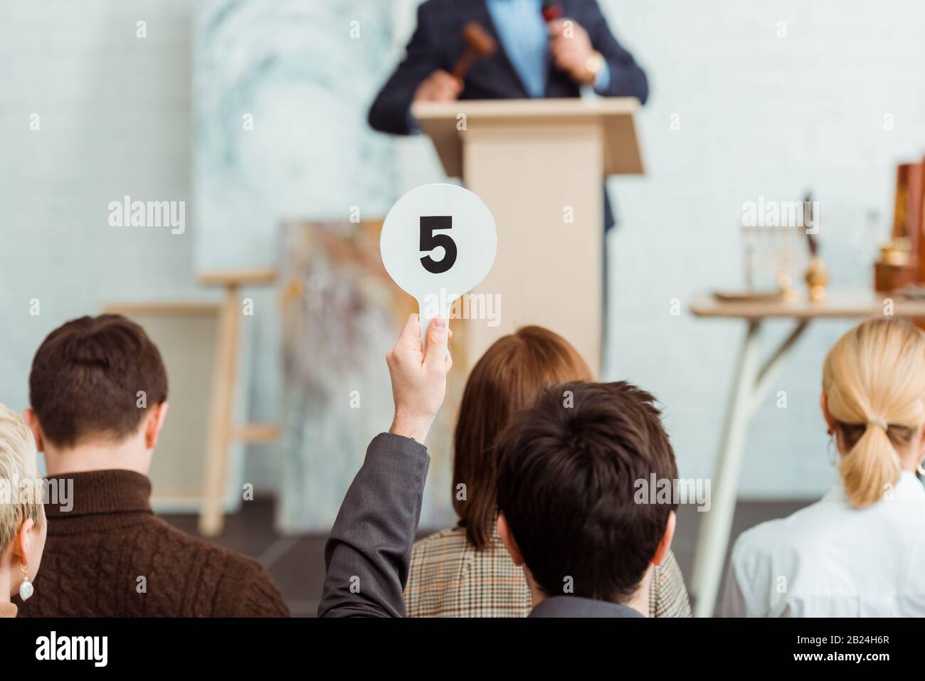 back view of buyer showing auction paddle with number five during auction Stock Photo