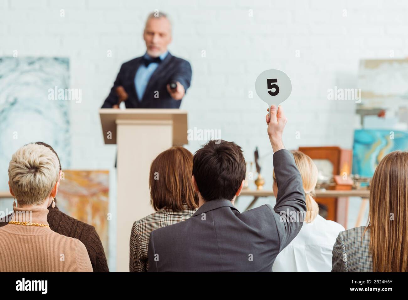 back view of buyer showing auction paddle with number five to auctioneer during auction Stock Photo