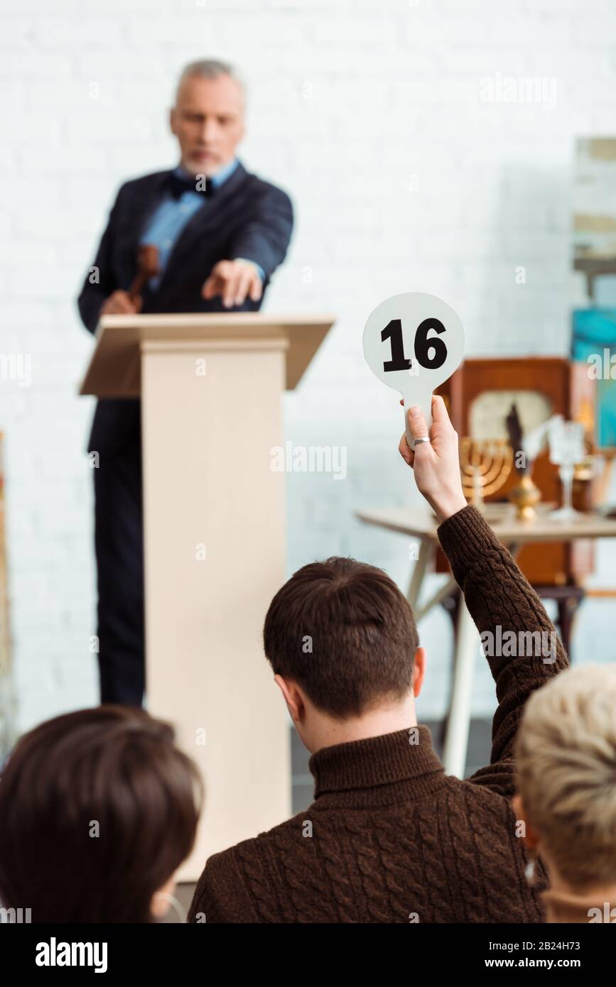 back view of buyer showing auction paddle with number sixteen to auctioneer during auction Stock Photo