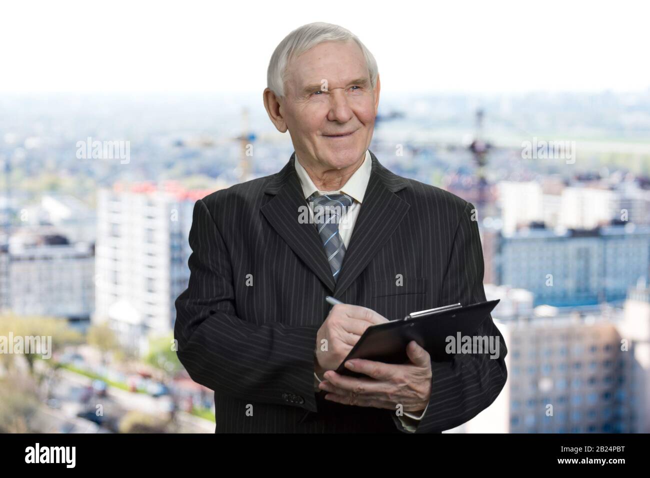 Old man in suit writing down on clipboard. Stock Photo