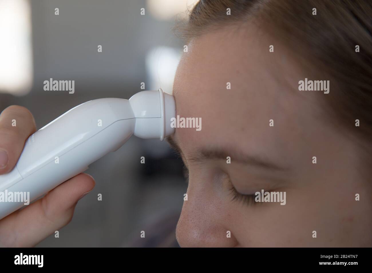 Girl using temporal artery thermometer, side view Stock Photo