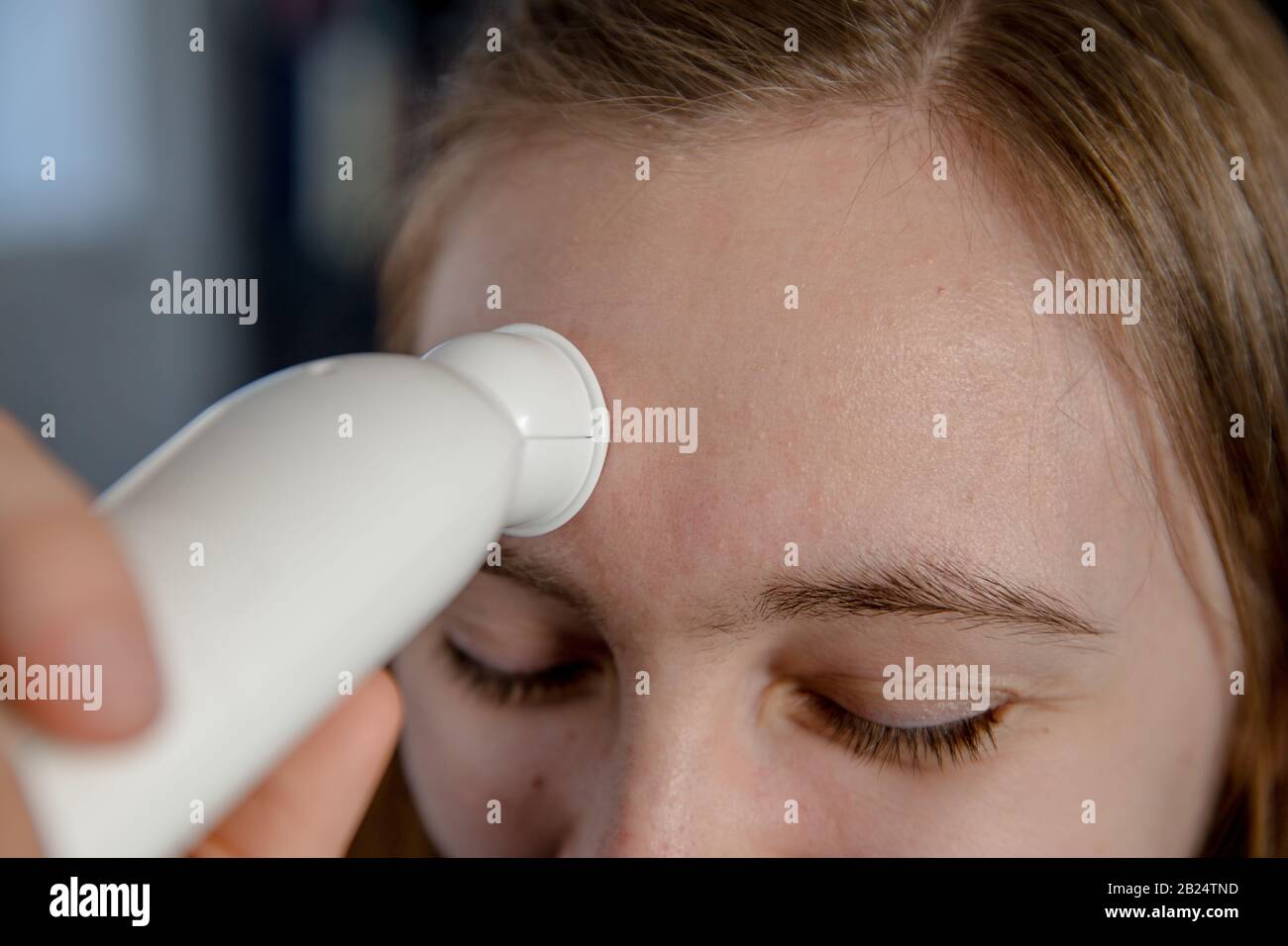 Girl using a temporal artery thermometer on her forehead Stock Photo