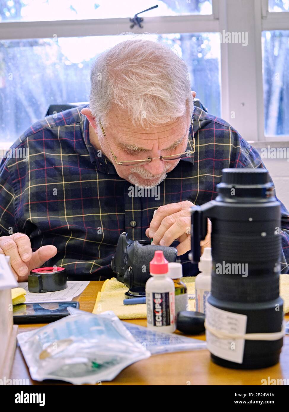Mature older man, technician, inspecting and cleaning a modern dslr camera or mirrorless camera sensor in Montgomery Alabama, USA. Stock Photo