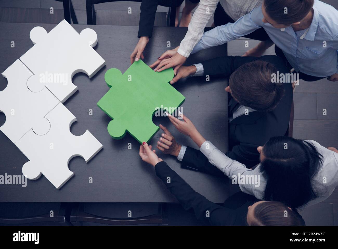 Group of business people assembling final piece of jigsaw puzzle, team work support and help