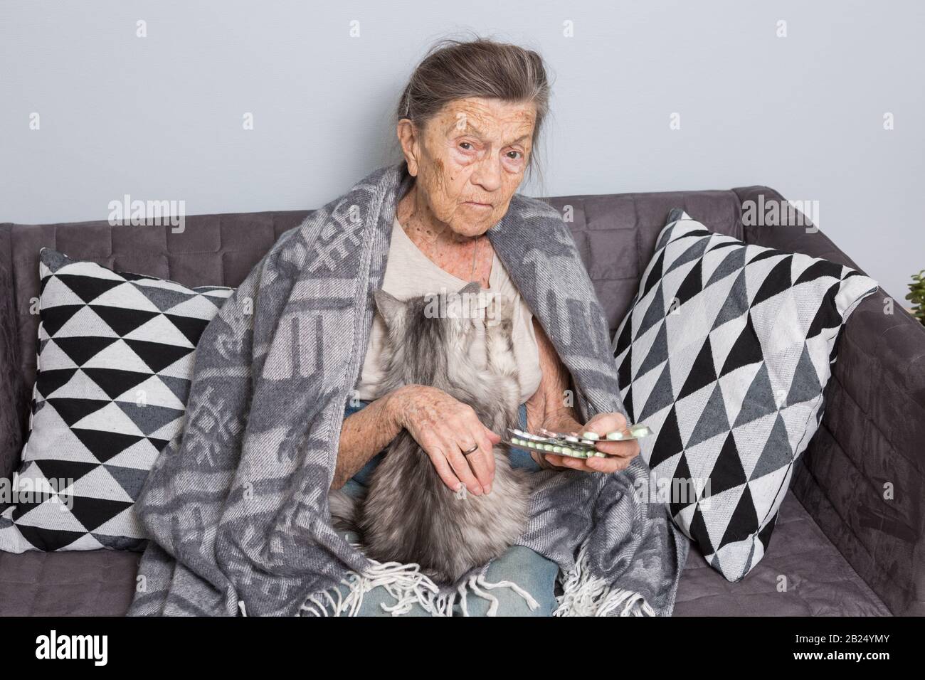 theme old age, loneliness health care. old grayhaired Caucasian woman with deep wrinkles sitting with pet animal cat. poor grandmother holding blister Stock Photo
