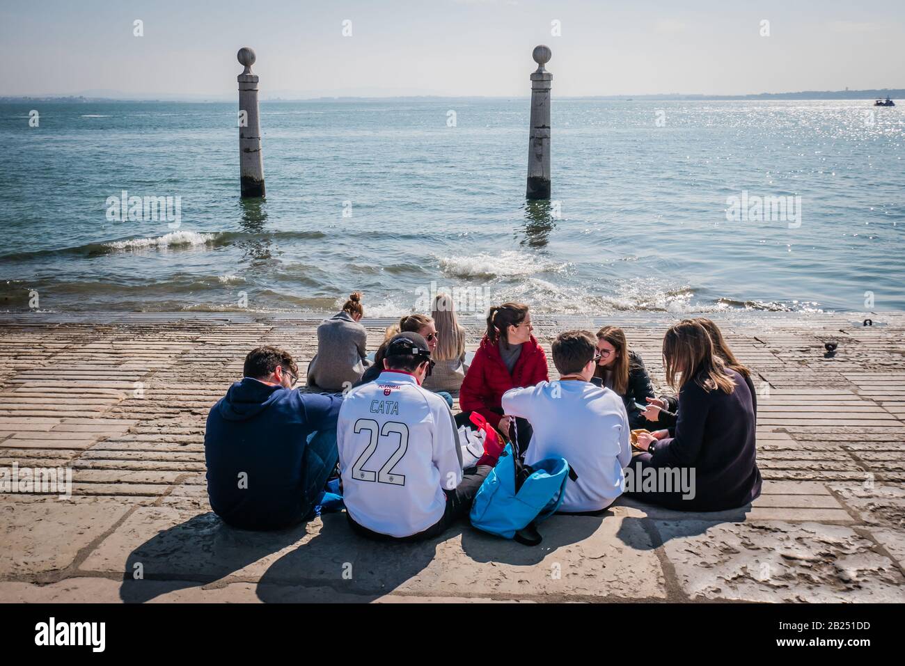 a group of teenagers gather by the tagus river in lisbon portugal on a sunny day during the winter season Stock Photo