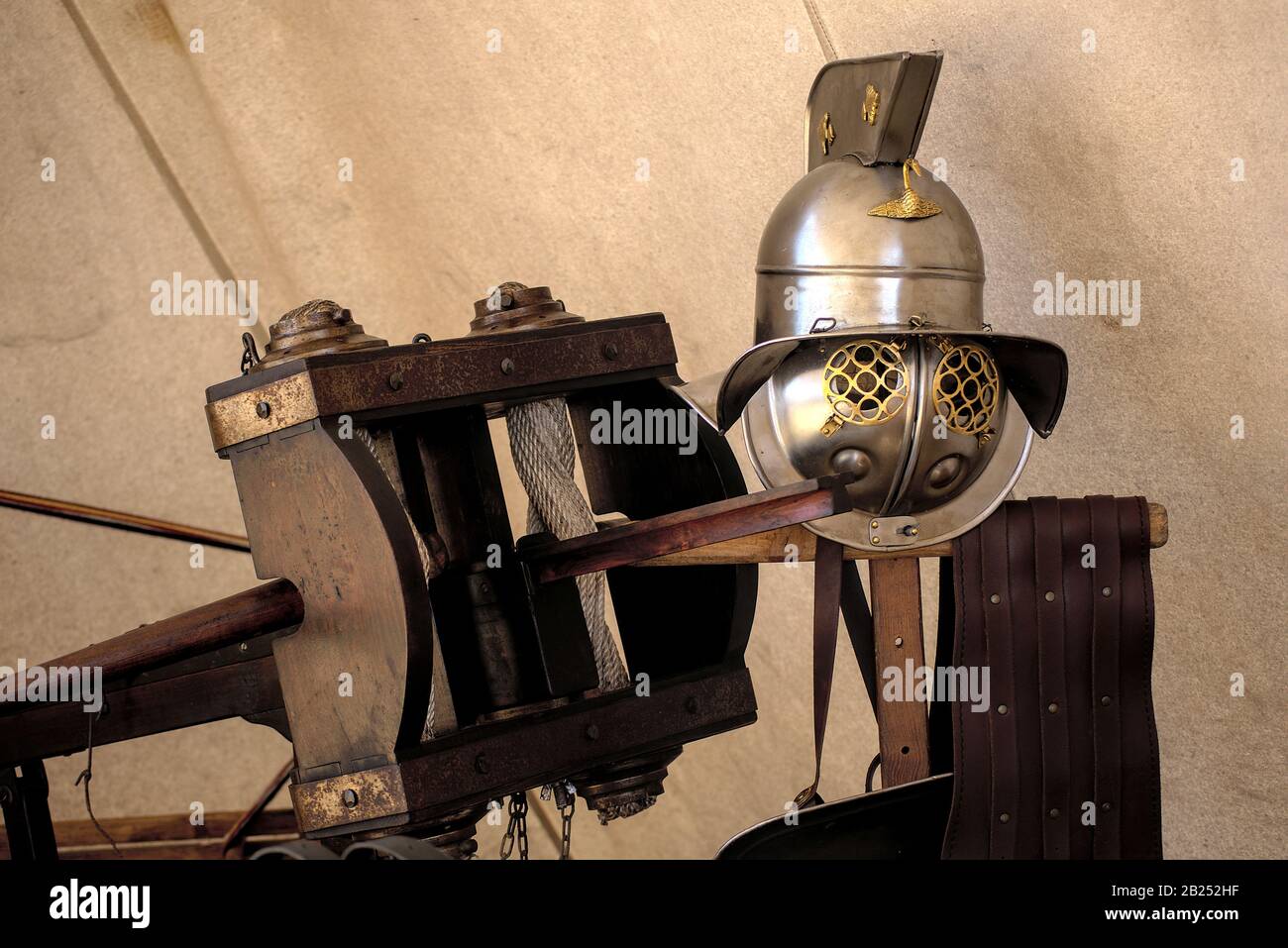 New looking Roman gladiators helmet on top of a wood pole with a traditional wood crossbow next to it Stock Photo