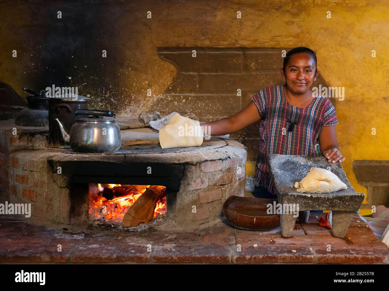 Smiling indigenous mexican woman with corn tortilla pancake making the traditional Tlayuda dish in colorful clothing by a fire, Oaxaca, Mexico. Stock Photo
