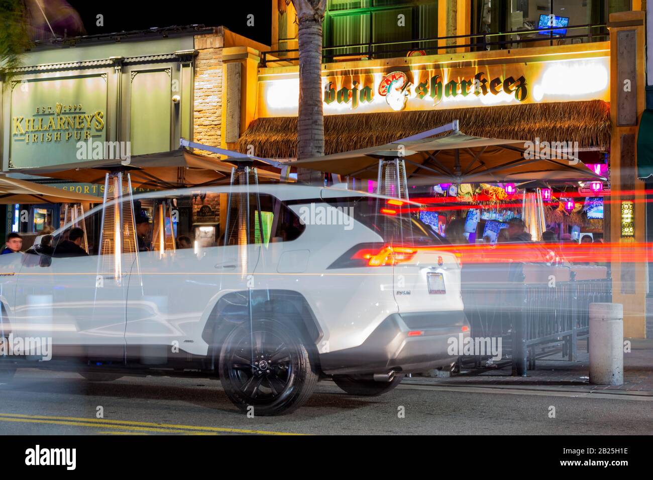 People having a fantastic time at restaurants and bars on a Saturday night on Main Street in Huntington Beach, with light trails and a ghosted car. Stock Photo