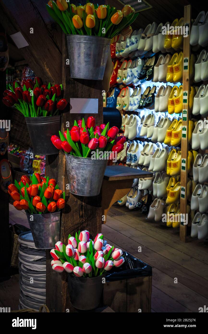 Magical colorful bouquets of wooden tulips in the metal bucket and wooden shoes in a row on the wall. Traditional souvenir shop decoration with handma Stock Photo