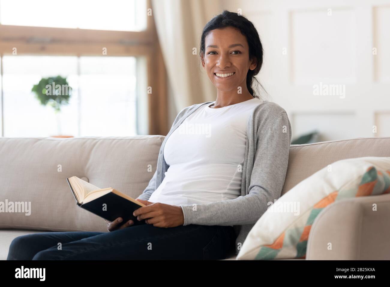 Portrait of smiling biracial woman relax on couch with book Stock Photo