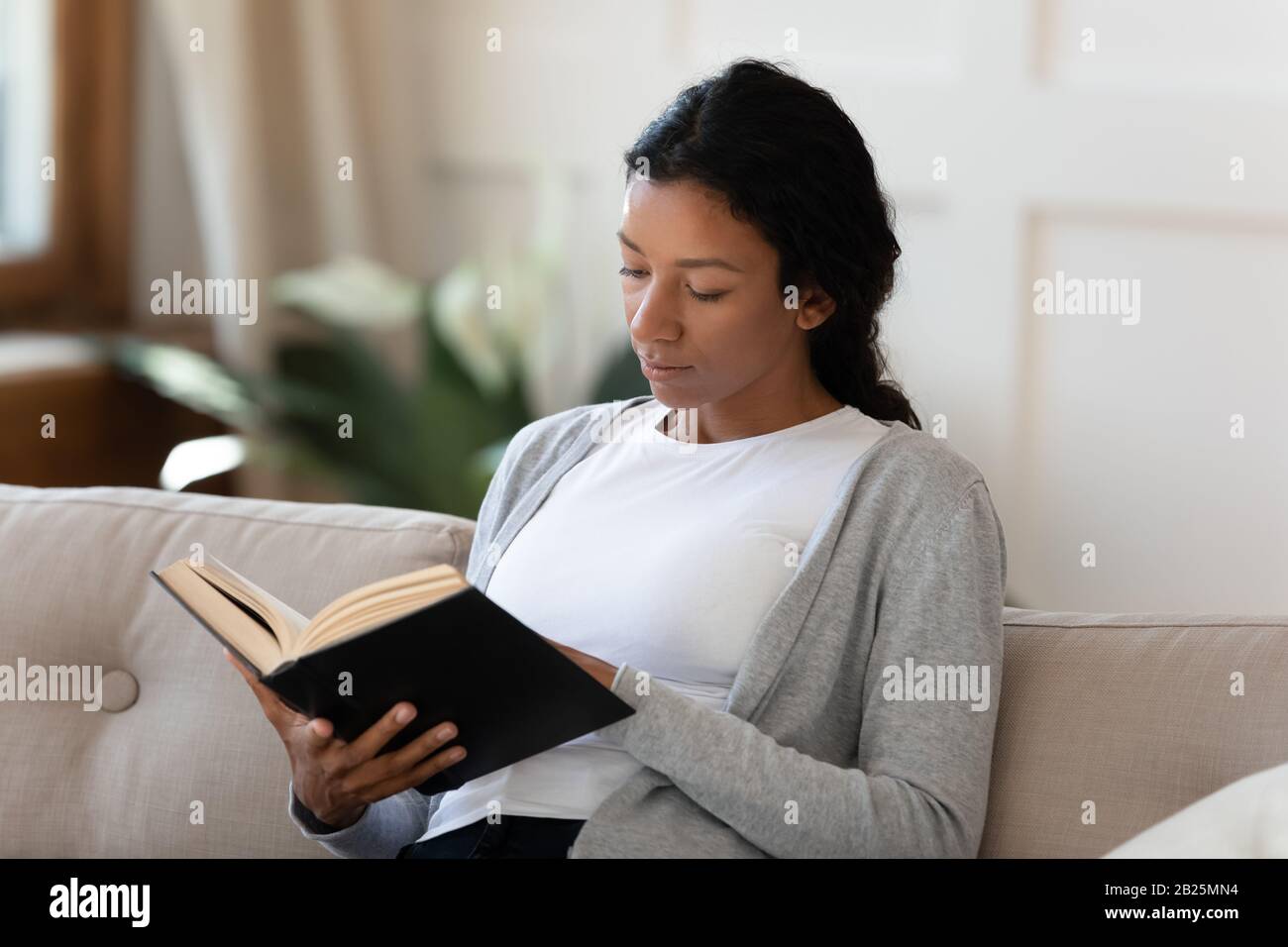African American woman relax on couch reading book Stock Photo