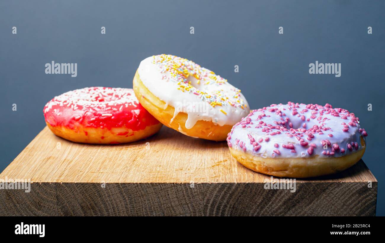 donuts with multi-colored red white and purple icing on a wooden stand on a gray background. Stock Photo