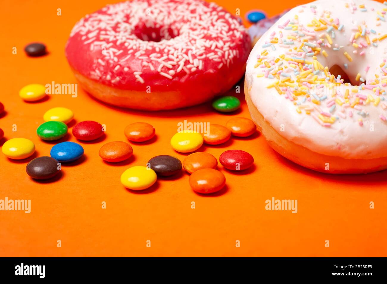 glazed red and white round bun donuts and multi-colored sweets on orange background. children's snacks. Stock Photo