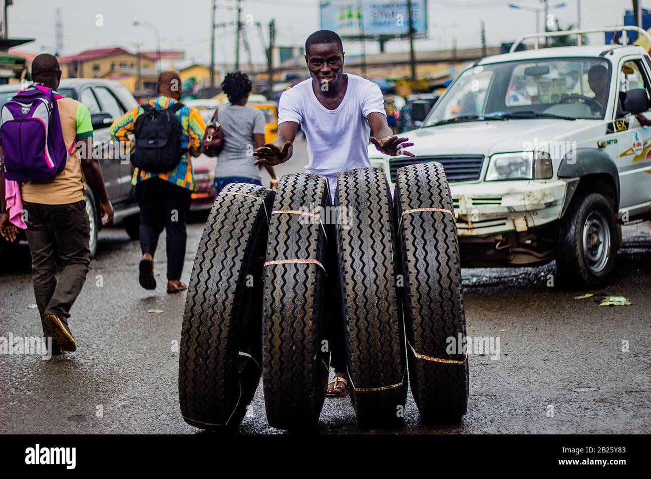 A tyre vendor rolls a bunch of tyres down the street at a market in Lagos, Nigeria Stock Photo