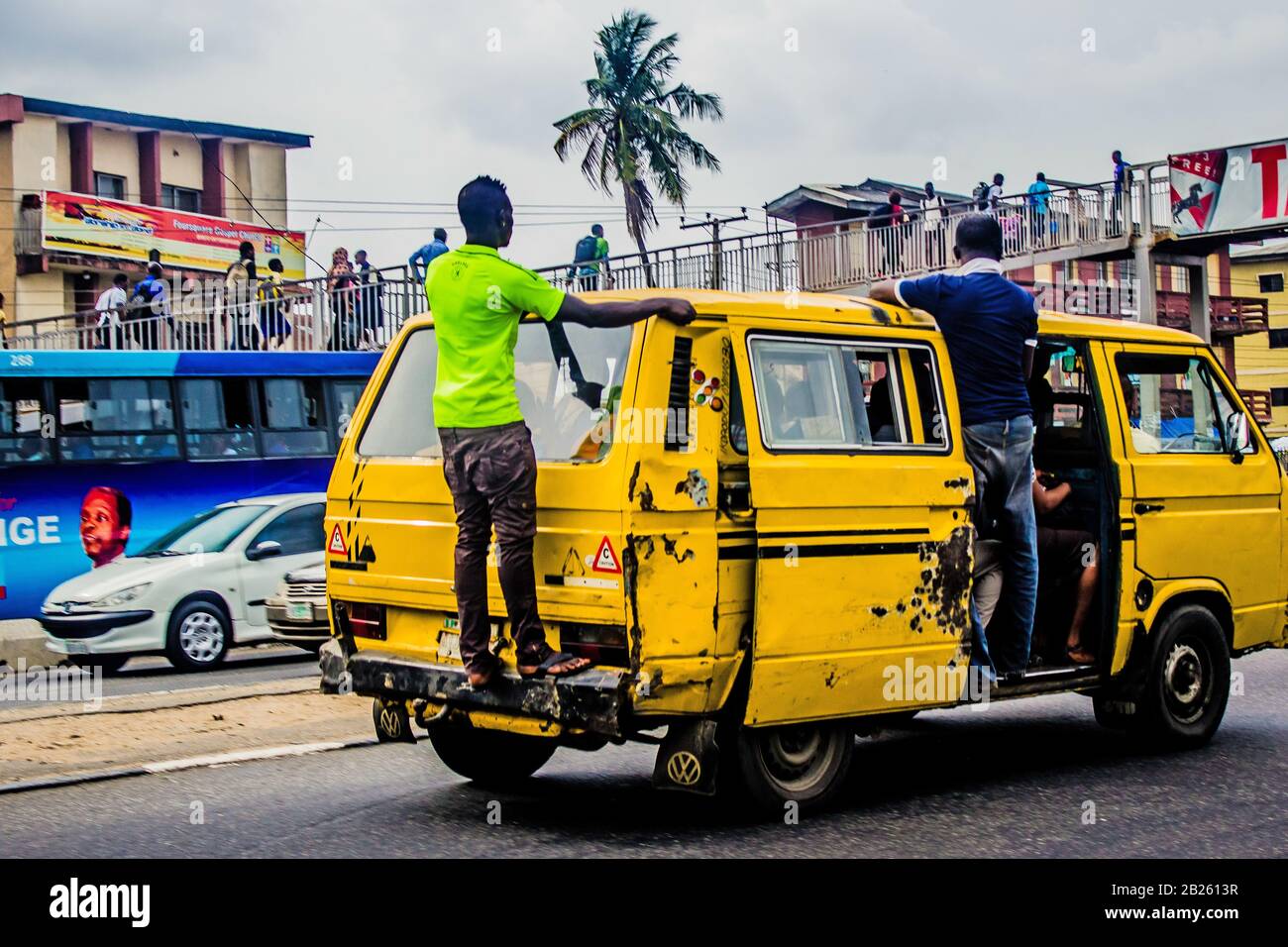 People hang of a bus (danfo) on a street in Lagos, Nigeria. Stock Photo