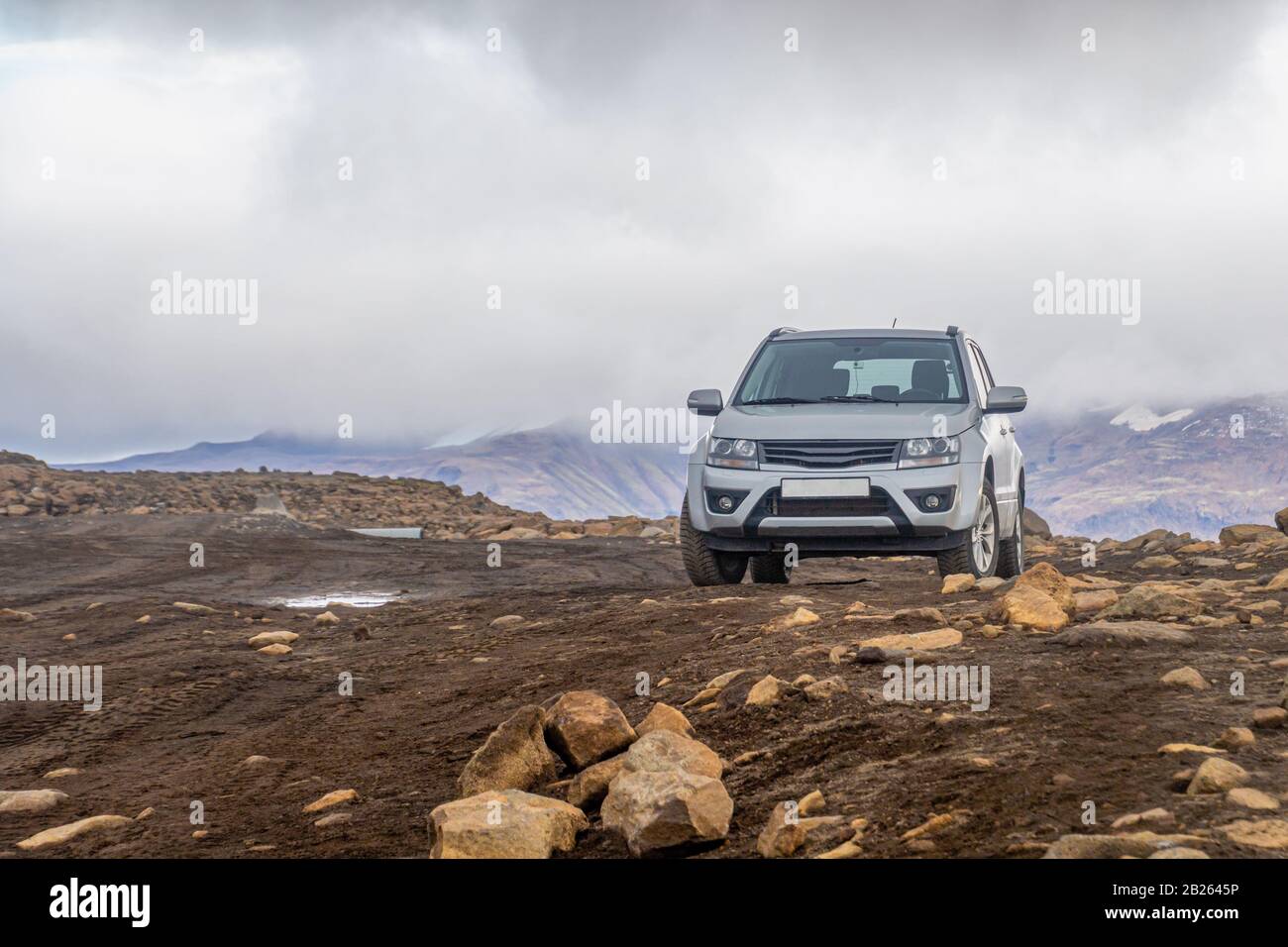 Langjokull Glacier SUV on muddy road standing between rocks in front of the mountain range Stock Photo