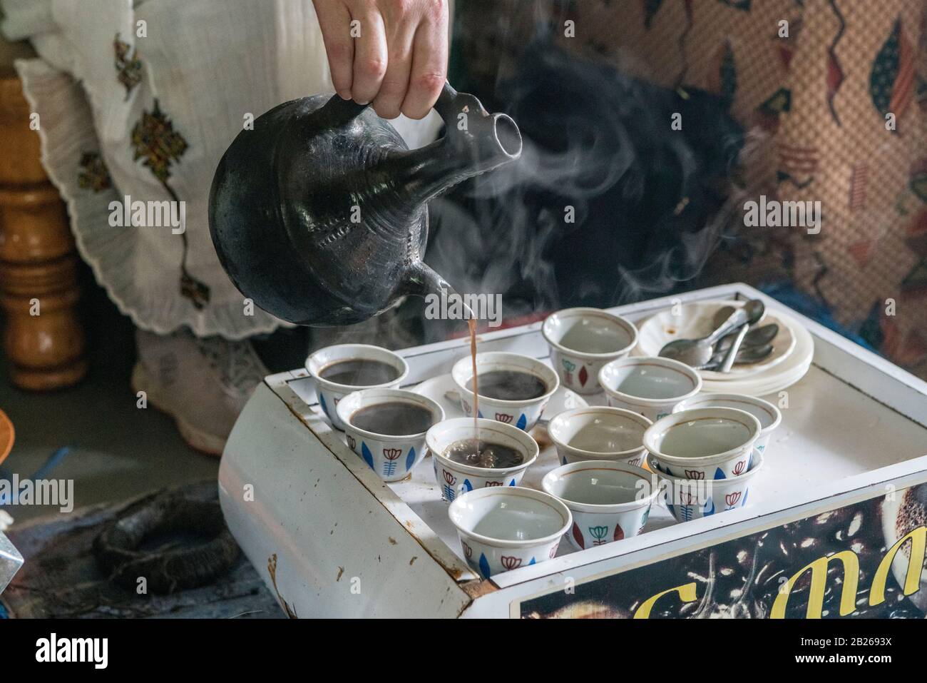 Woman pouring traditionally brewed coffee into finjal - coffee cup - from a jebena - coffee pot in a house in southern Ethiopia Stock Photo