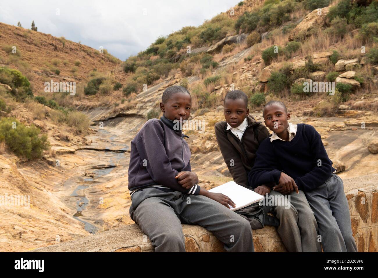 School boys doing homework on the walking bridge crossing the Liphiring River to the Ha Baroana rock paintings, Lesotho Stock Photo