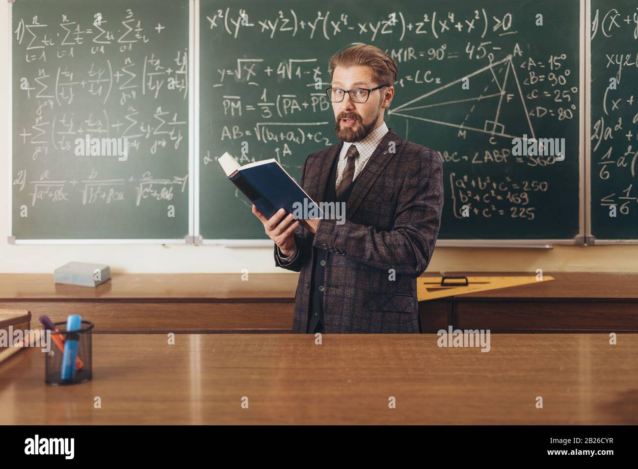 Bearded professor in suit and glasses citing a manual to explain the math lecture material Stock Photo