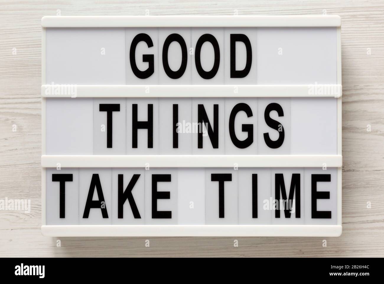 'Good things take time' words on a lightbox on a white wooden background, top view. Overhead, from above, flat lay. Stock Photo