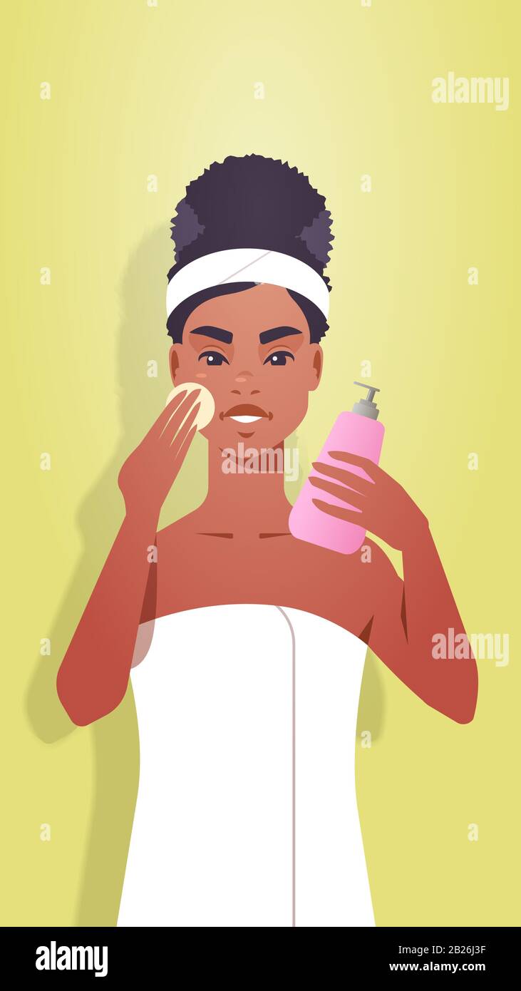 young woman applying foundation cream dressed in towel african american