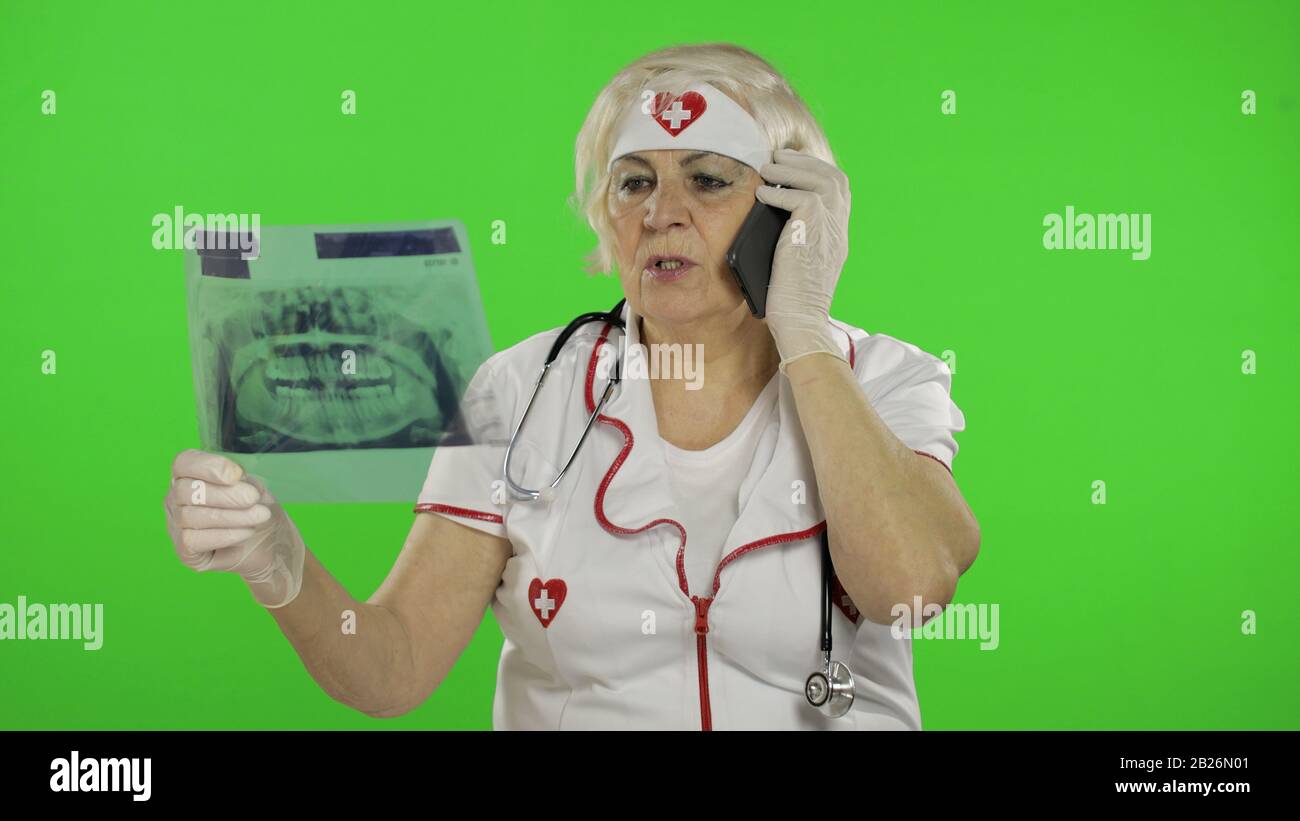 Portrait of elderly caucasian female doctor talking on the phone with client. Female nurse with radiogram, x-ray. Dentist. Green screen. Chroma key Stock Photo