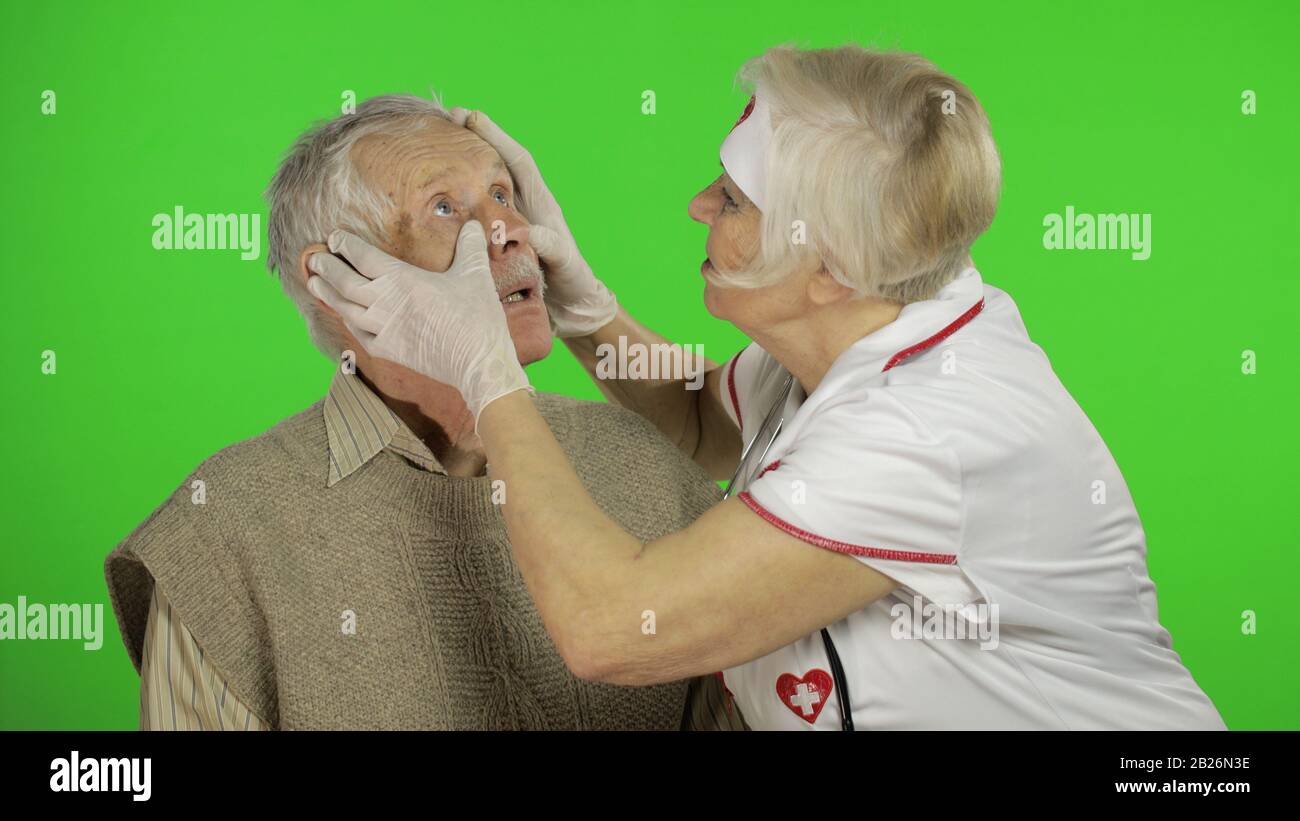 Kind mature woman nurse caregiver supporting to old elder man help with problem, female doctor therapist in uniform examines man and give treatment tips to senior patient Stock Photo