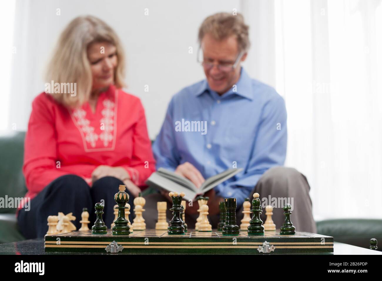 Mature couple reading a book in a bright living room - focus on the chessmen in the foreground Stock Photo