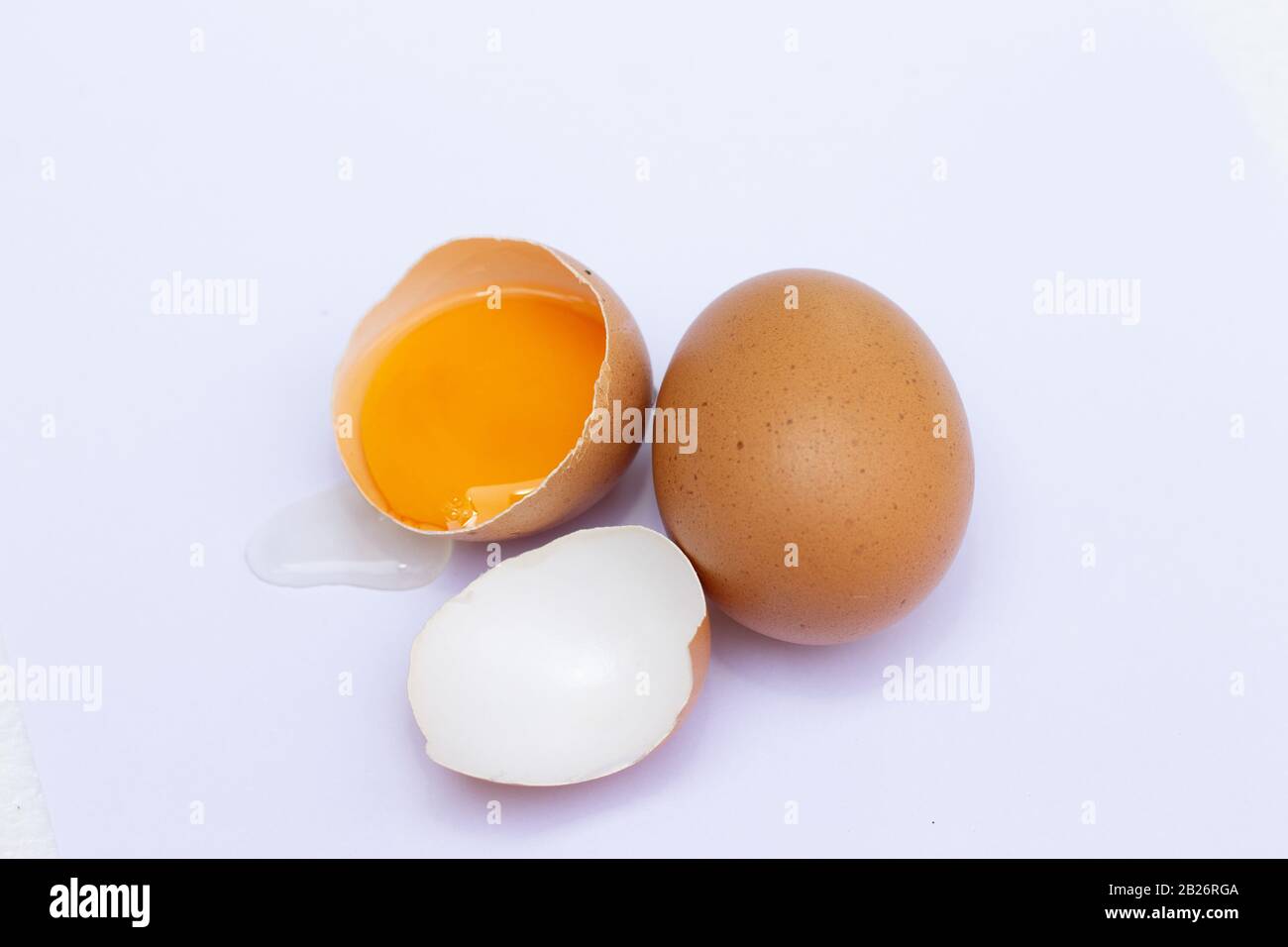 Two brown eggs There was one egg broken in half, with a yolk inside the eggshell and the egg whites flowing on a white background. Stock Photo